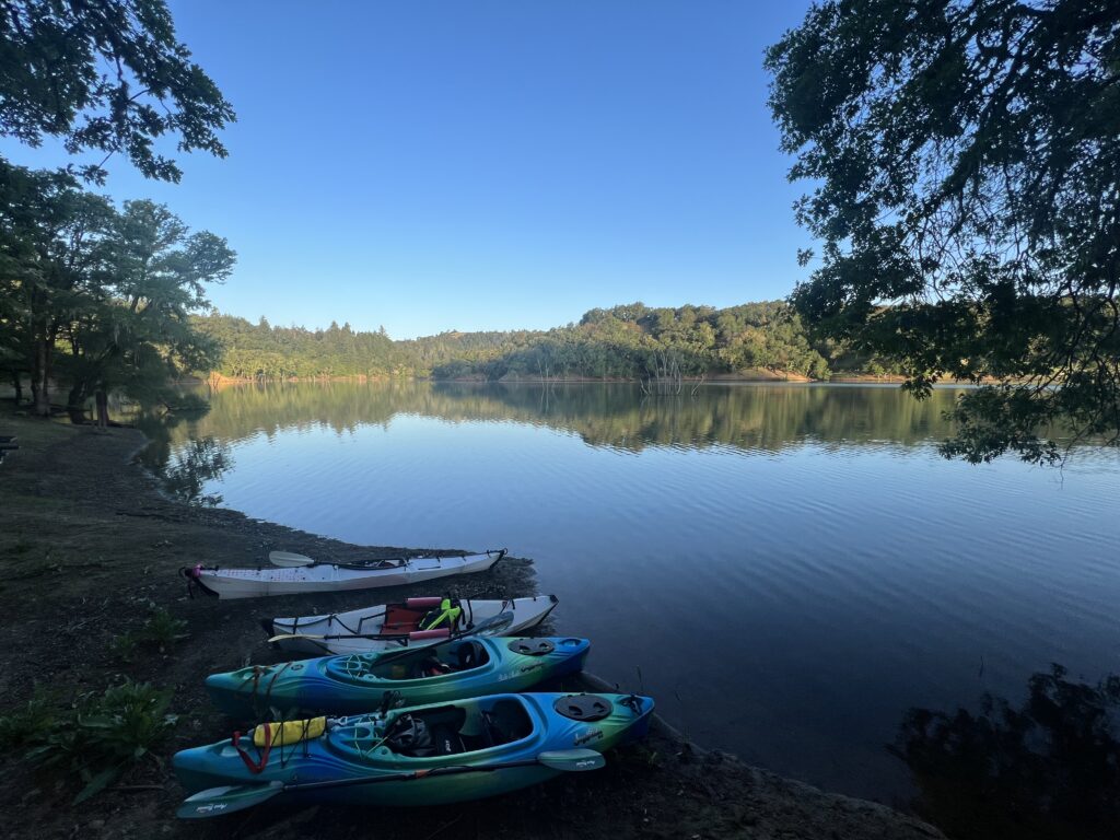 Photo showing four kayaks on the shore of Thumb camp on Lake Sonoma at sunset with still water.