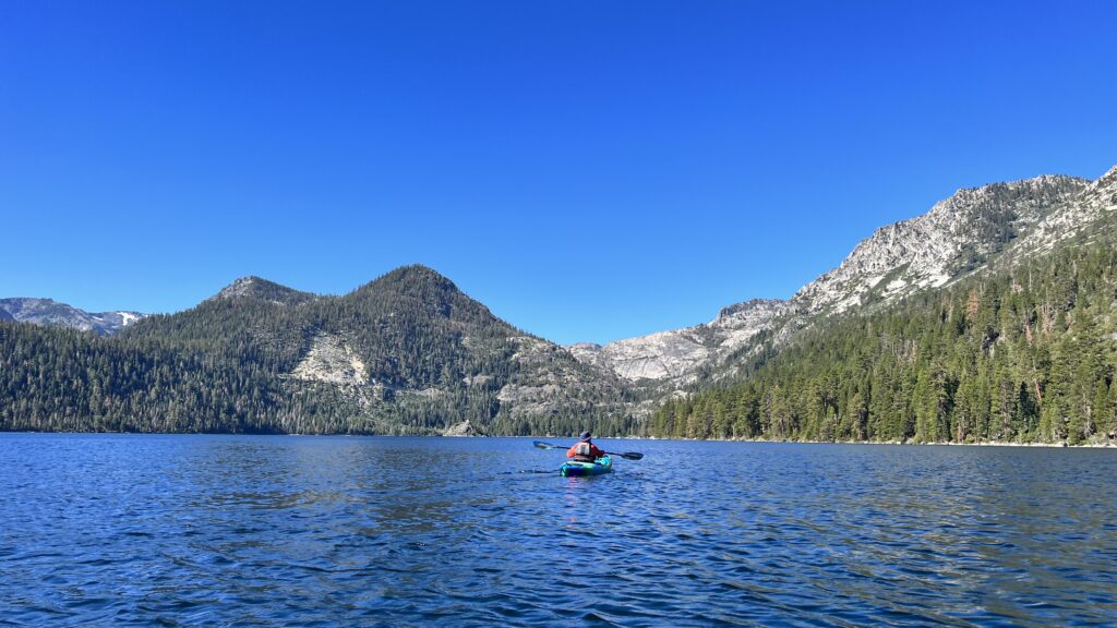 Photo of a kayaker paddling into Emerald Bay surrounded by huge mountains.  Kayak camping in Emerald Bay is a bucket list item for many California paddlers. 